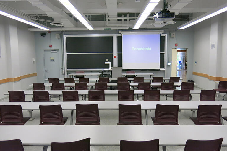 Etcheverry 3107 has five rows of connected desks and fixed chairs with a moveable speaker podium facing the class. The moveable document camera is in the front of the classroom. The AV rack/blackbox is in the back of the classroom. There is one projector