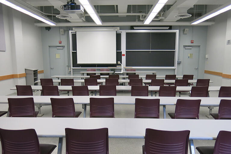 Etcheverry 3111 has five rows of connected desks and fixed chairs with a moveable speaker podium. The moveable document camera is in the front of the classroom. The AV rack/blackbox is in the back of the classroom. There is one projector screen that cover
